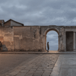 Diferença entre moral e ética: cena panorâmica contínua mostrando vizinhança brasileira com moradores conversando, transição por arco de pedra e colunas clássicas com filósofo e pergaminhos.