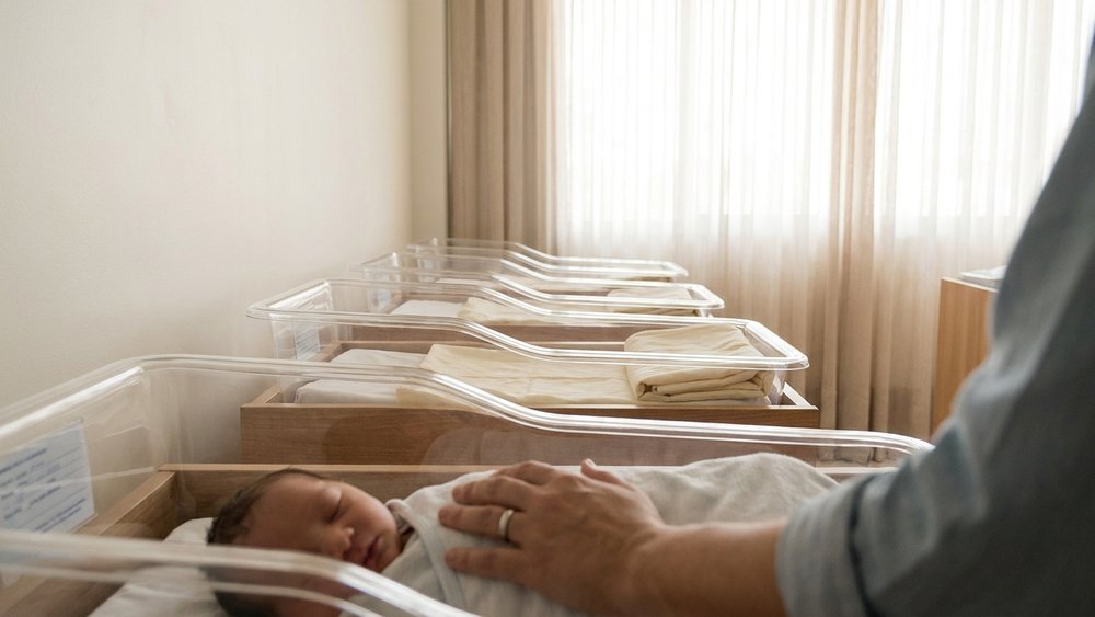nomes bíblicos — berçário de maternidade brasileira com a mão de um dos pais sobre um bebê adormecido em luz suave